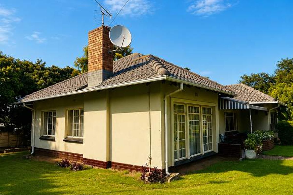 Rear view of a single-story house featuring a tiled roof, brick chimney, and a well-maintained lawn area.