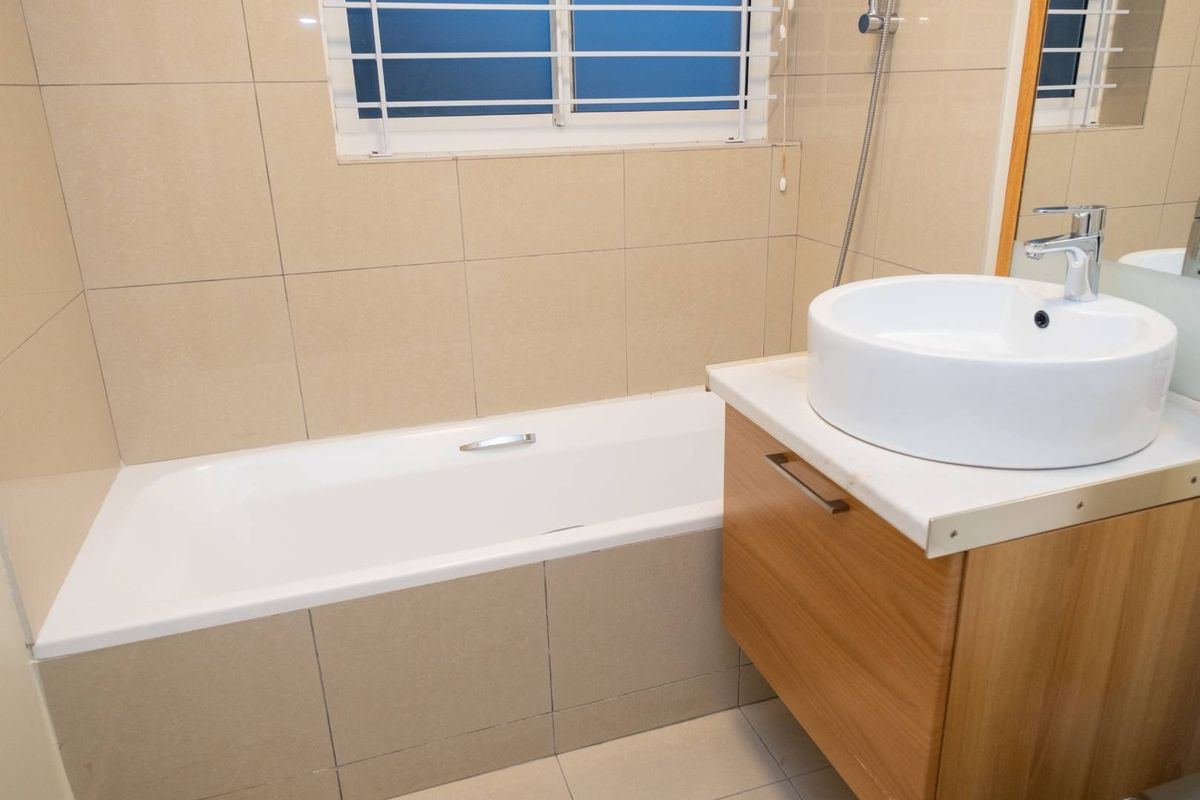 A clean, modern bathroom featuring a built-in bathtub, a wooden vanity cabinet with a vessel sink, and neutral wall and floor tiling.