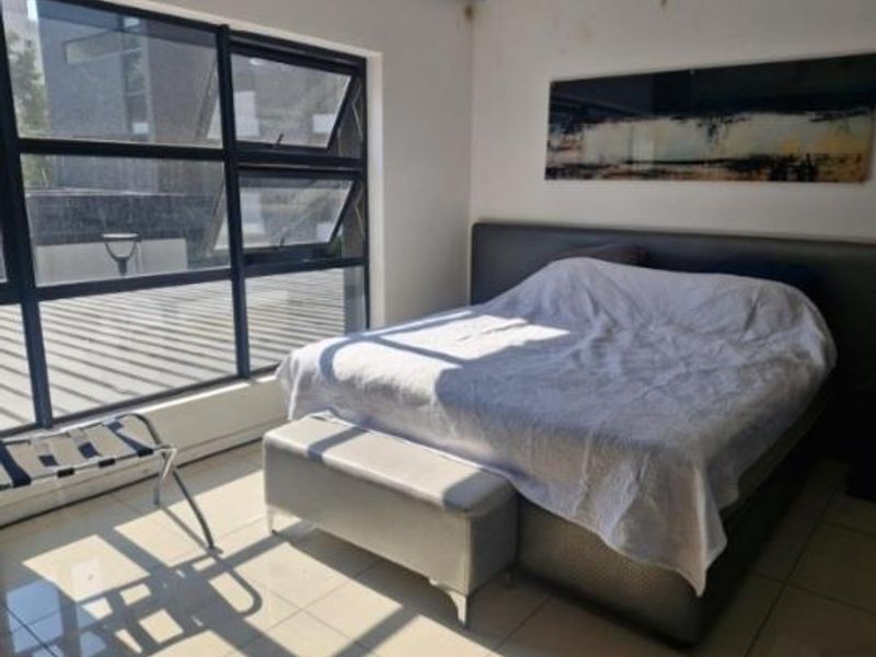 A bedroom featuring large aluminium-framed windows providing natural light and tiled flooring, with visible ceiling water damage requiring attention.