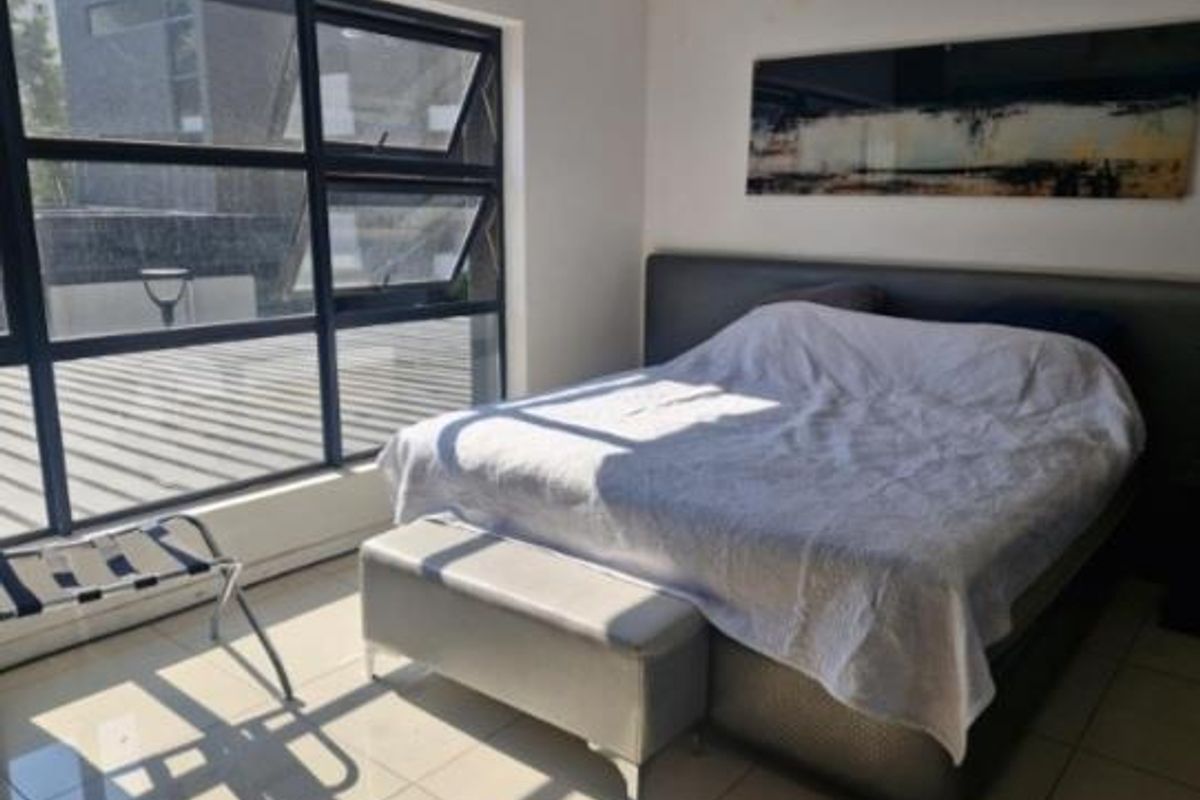 A bedroom featuring large aluminium-framed windows providing natural light and tiled flooring, with visible ceiling water damage requiring attention.