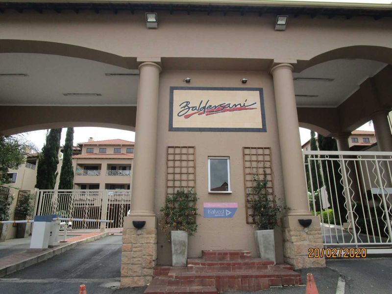 The main entrance gate and security access point for the Baldersani apartment complex, featuring stone-clad columns and gated vehicle access.