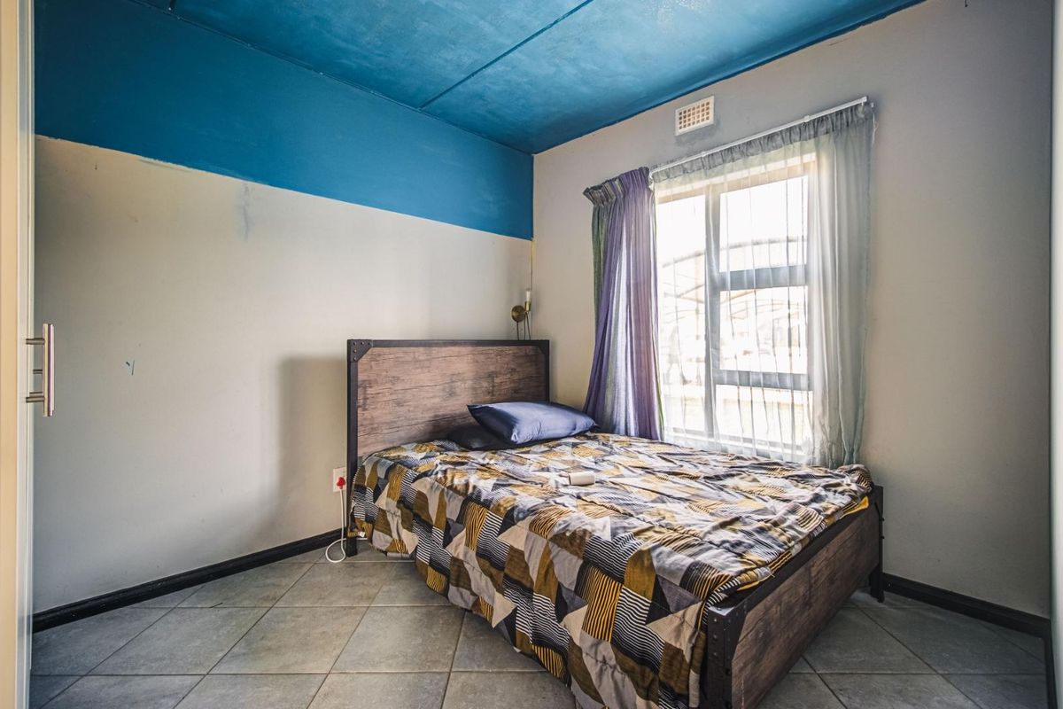 A bedroom featuring tiled flooring and an aluminium window. The room requires cosmetic updates to the wall finishes to improve its overall appeal.