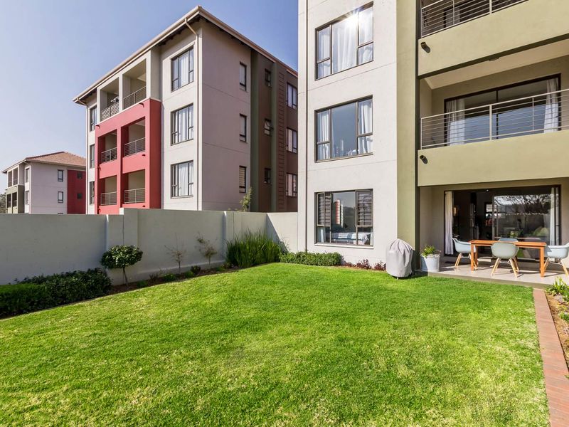 A well-maintained rear garden area featuring a manicured lawn, boundary wall, and a paved patio space connected to the apartment via sliding glass doors.