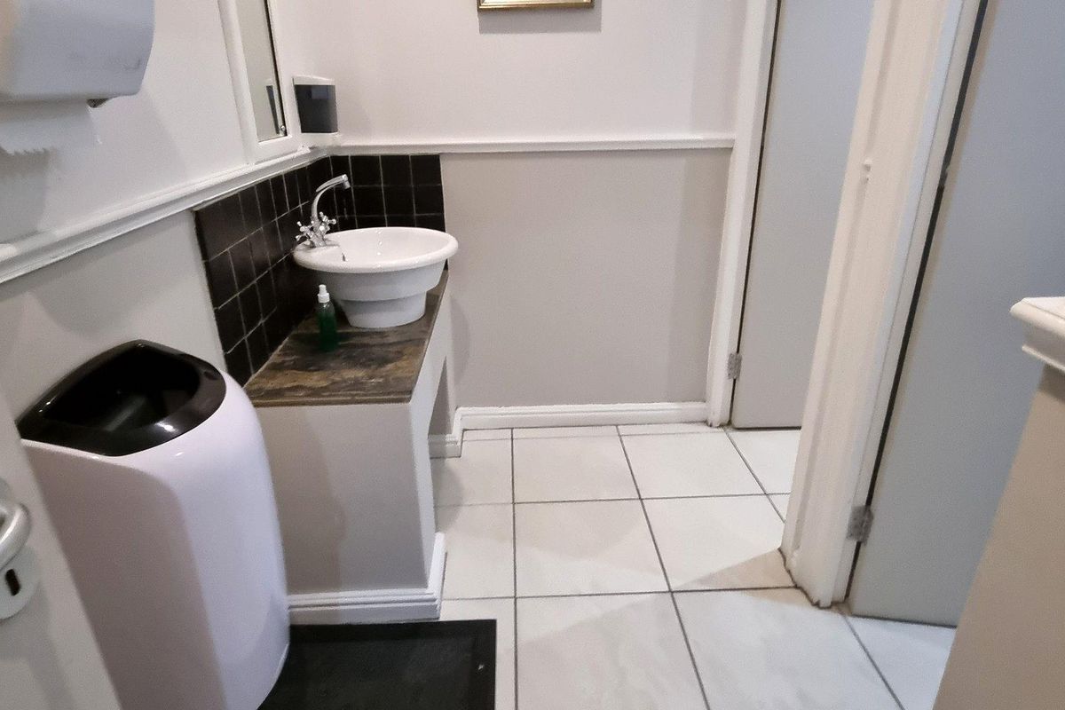A functional office restroom featuring a pedestal-style basin, tiled splashback, and ceramic floor tiles.