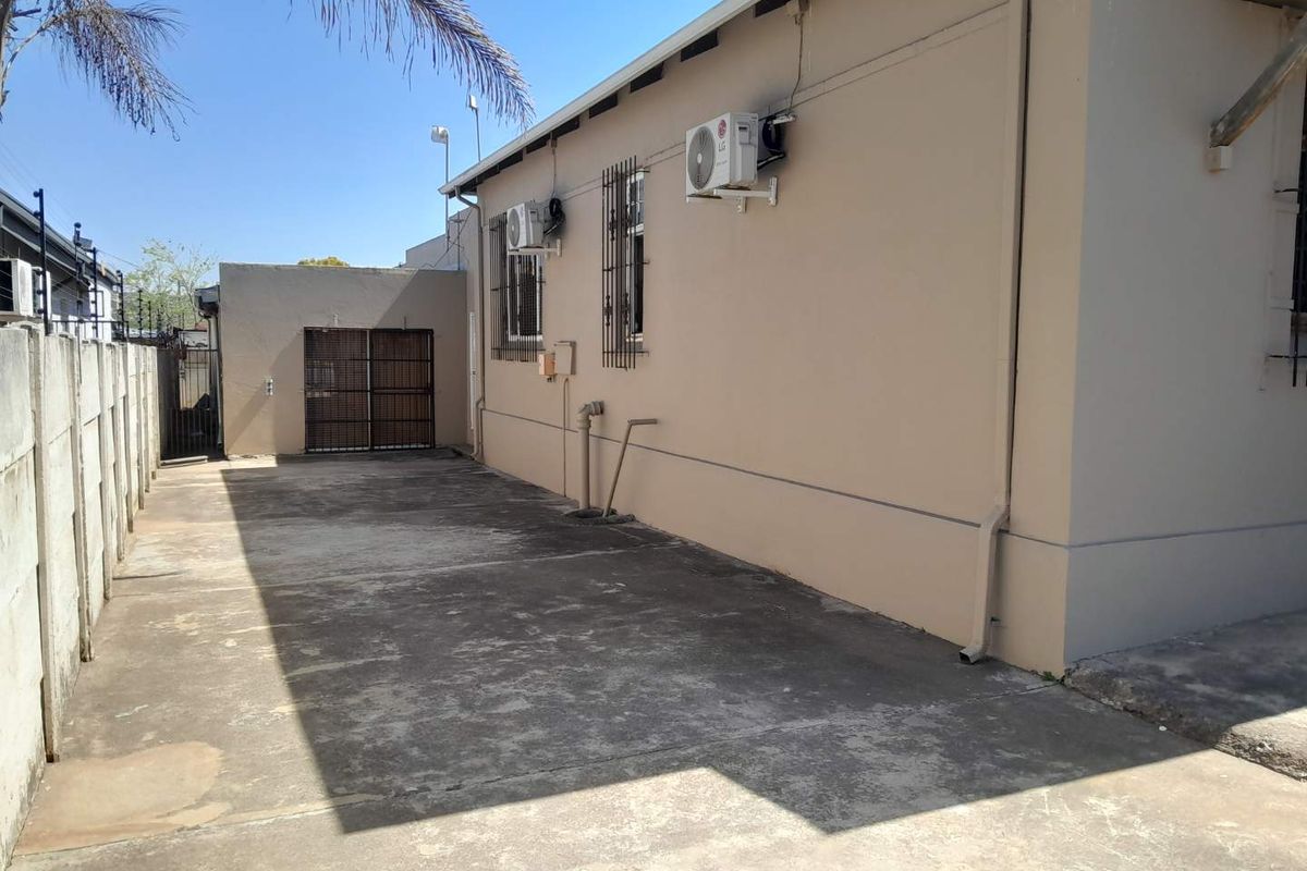 A side exterior view of the business property featuring concrete paving, security bars on windows, and wall-mounted air conditioning units.