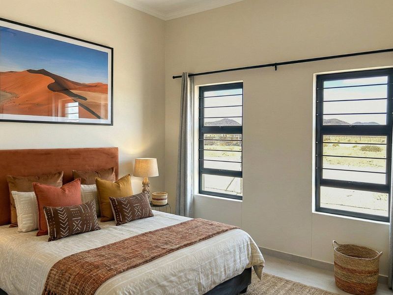 A well-maintained bedroom featuring louvered windows with security bars, neutral tiled flooring, and a clean, modern aesthetic.