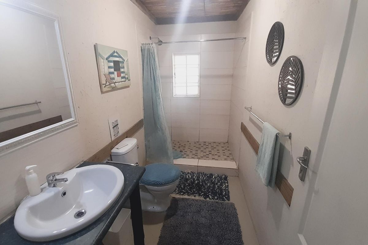A functional bathroom featuring a walk-in shower with curtain, pedestal basin, and toilet, finished with neutral wall tones and tiled flooring.