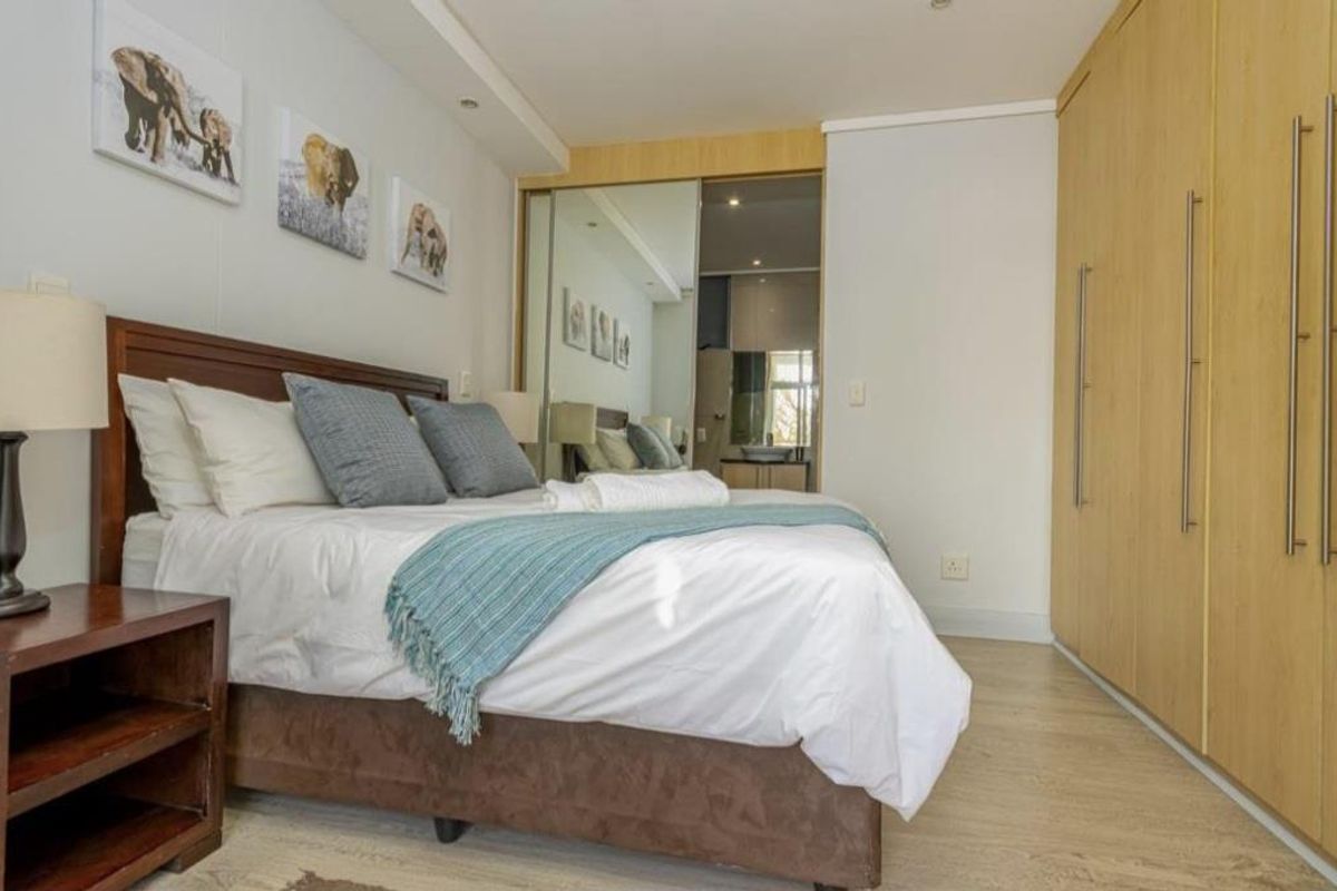 A well-maintained bedroom featuring built-in wooden cupboards, light wood-look flooring, and an en-suite bathroom with a mirrored door.
