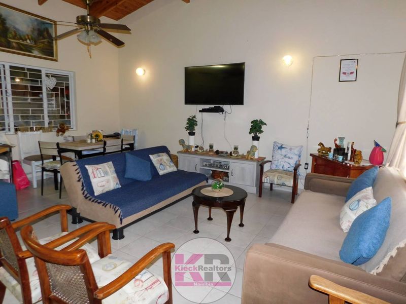 A spacious living room featuring tiled flooring, exposed timber ceiling beams, and a ceiling fan, offering a comfortable and functional family living space.