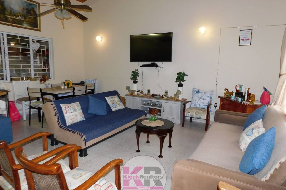 A spacious living room featuring tiled flooring, exposed timber ceiling beams, and a ceiling fan, offering a comfortable and functional family living space.
