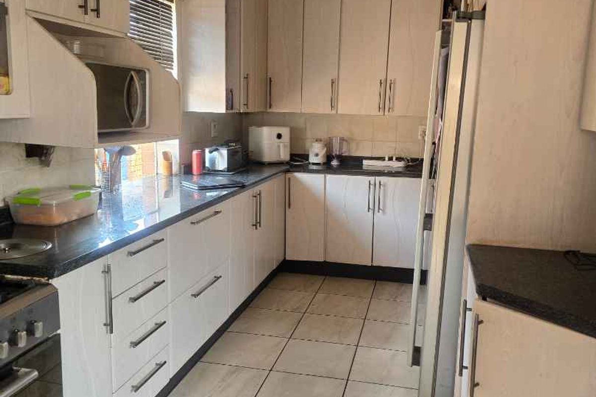 A functional kitchen featuring light-toned cabinetry, dark countertops, tiled flooring, and integrated appliance spaces, offering a practical layout for daily meal preparation.
