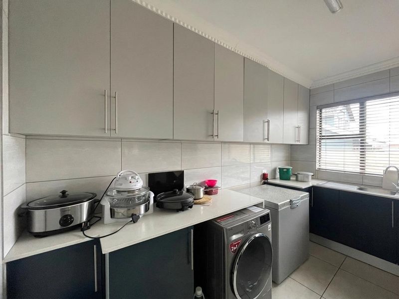 A functional laundry room featuring modern grey cabinetry, tiled backsplash, and tiled flooring with space for laundry appliances and a sink.