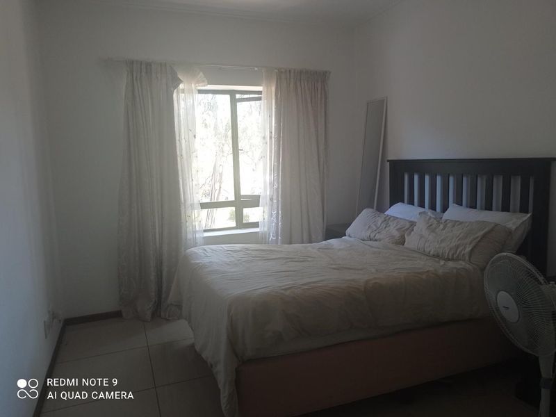 A simple bedroom featuring tiled flooring and a large window with natural light, providing a functional and neutral living space.
