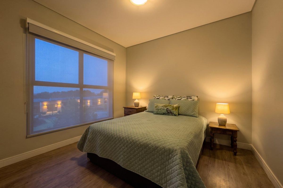 A well-maintained bedroom featuring laminate flooring, neutral wall tones, and a large window with a roller blind.