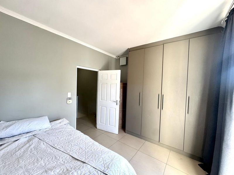 A well-maintained bedroom featuring neutral grey walls, large built-in cupboards, and light-colored floor tiles.