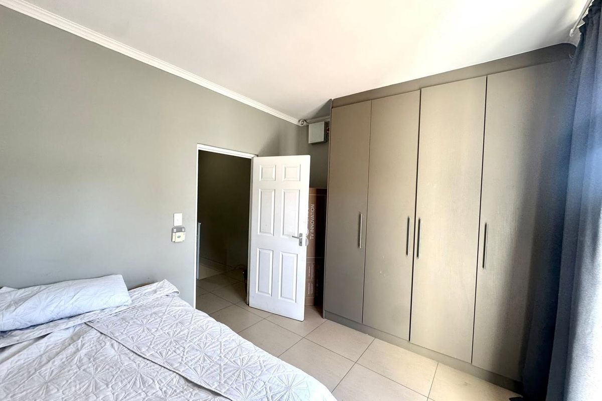 A well-maintained bedroom featuring neutral grey walls, large built-in cupboards, and light-colored floor tiles.