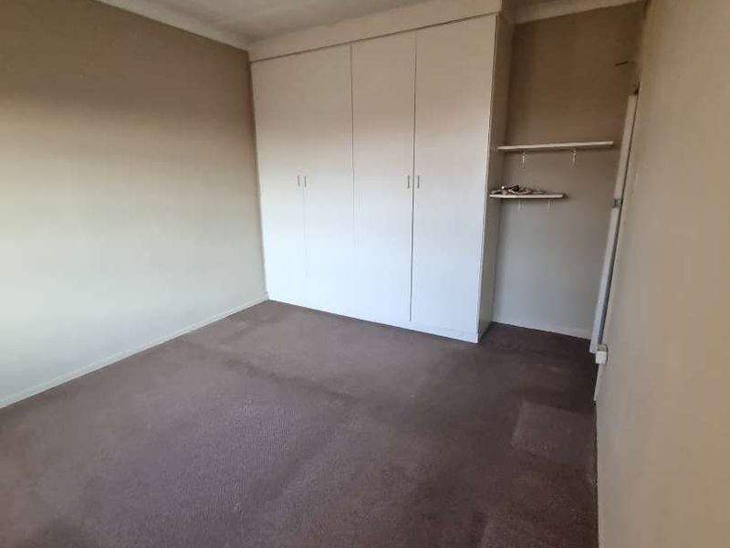 An empty bedroom featuring built-in cupboards, carpeted flooring, and a neutral color palette, ready for personalization.