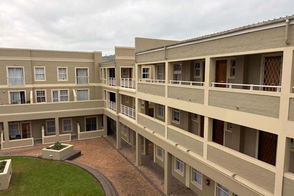 An elevated view of the apartment complex courtyard, featuring brick-paved walkways, a central lawn area, and multi-level exterior access corridors with security balustrades.