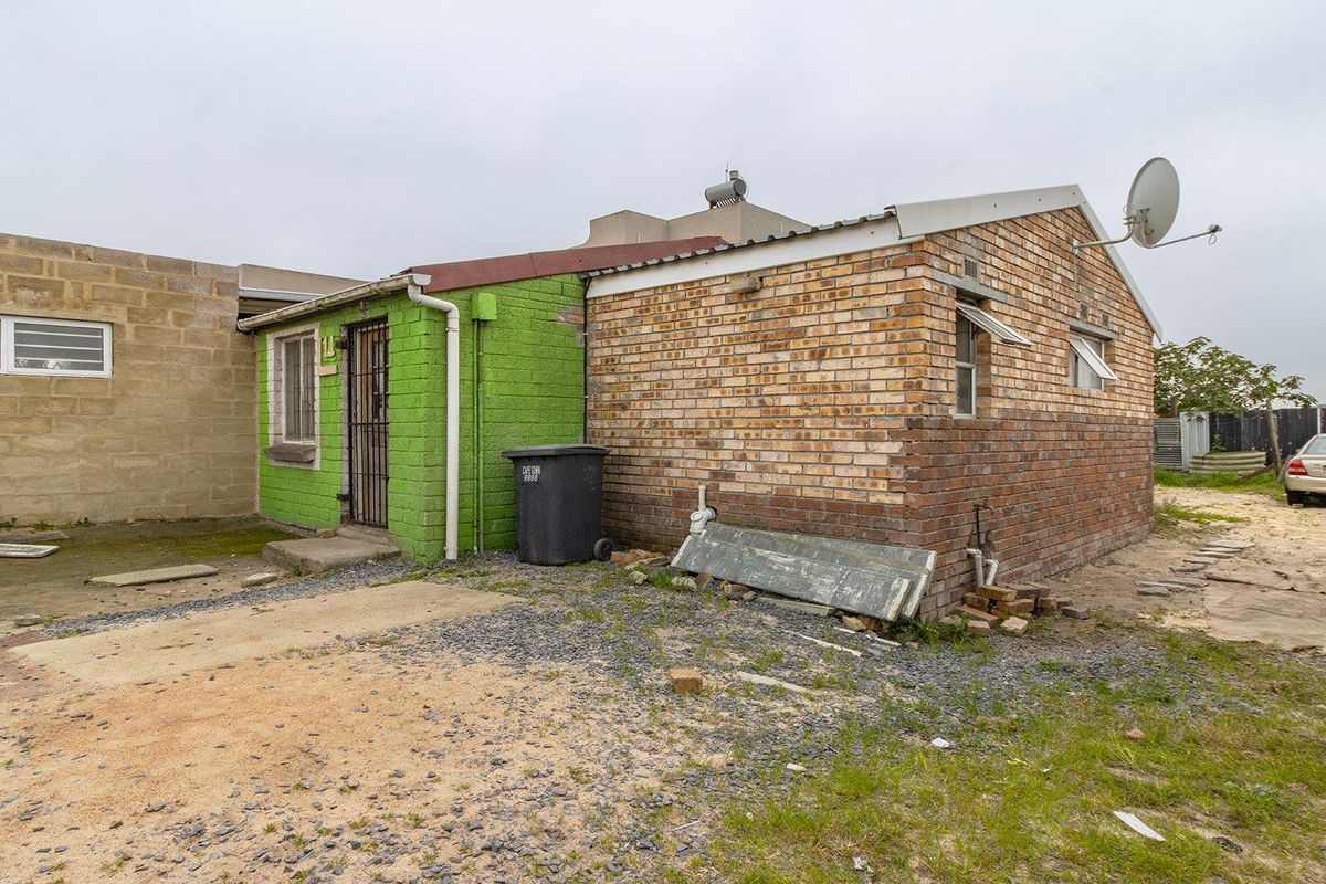 Rear view of a brick house featuring a security gate, solar water heater, and satellite dish, set on an unpaved yard.