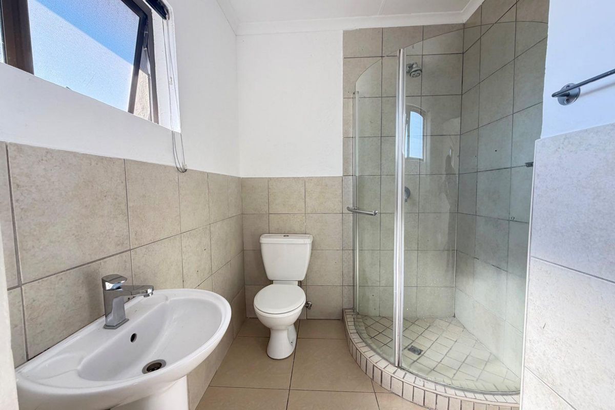 A functional bathroom featuring a pedestal basin, a toilet, and a curved glass shower enclosure with neutral wall and floor tiling.