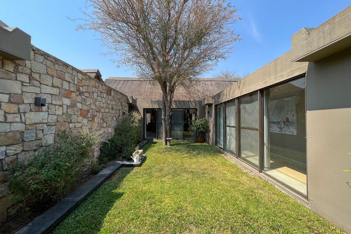 A private rear courtyard garden featuring a natural stone feature wall, manicured lawn, and large glass sliding doors providing seamless indoor-outdoor flow.