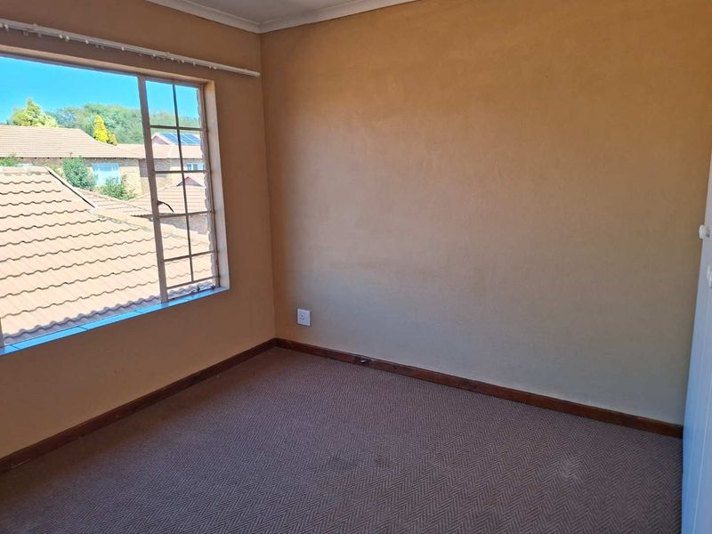 An empty bedroom featuring carpeted flooring, neutral wall tones, and a window providing natural light and a view of the surrounding neighborhood.