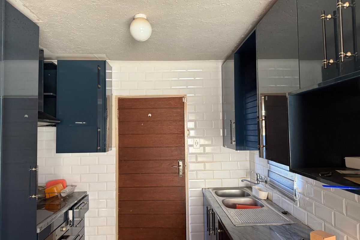 A compact kitchen featuring modern glossy blue cabinetry, white subway tile backsplash, stone countertops, and a double bowl stainless steel sink.