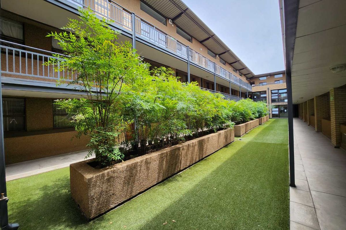 A well-maintained apartment complex courtyard featuring artificial turf, integrated concrete planter boxes, and covered walkways providing access to residential units.