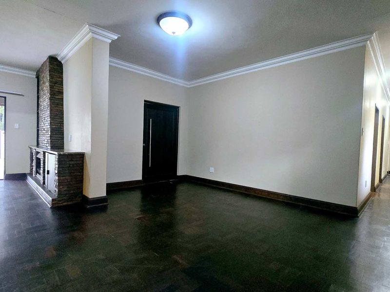 Spacious living area featuring classic parquet flooring, crown molding, and a distinctive stone fireplace, leading to a hallway and outdoor access.