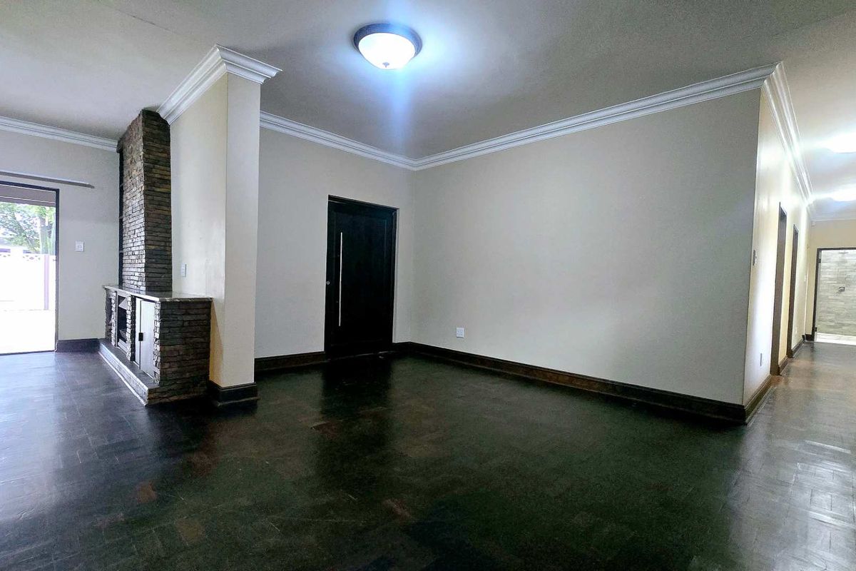 Spacious living area featuring classic parquet flooring, crown molding, and a distinctive stone fireplace, leading to a hallway and outdoor access.