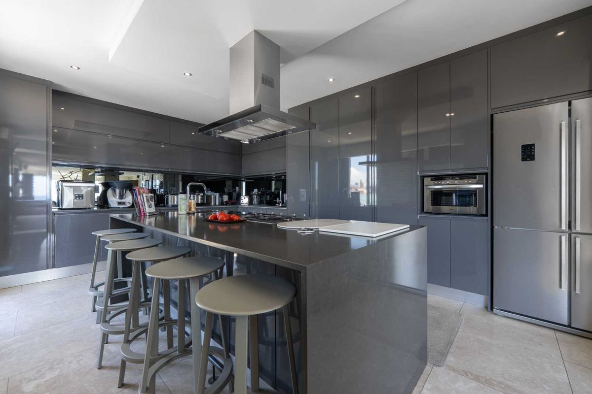 Modern kitchen featuring high-gloss grey cabinetry, a large central island with stone countertops, integrated appliances, and a sleek mirror splashback.