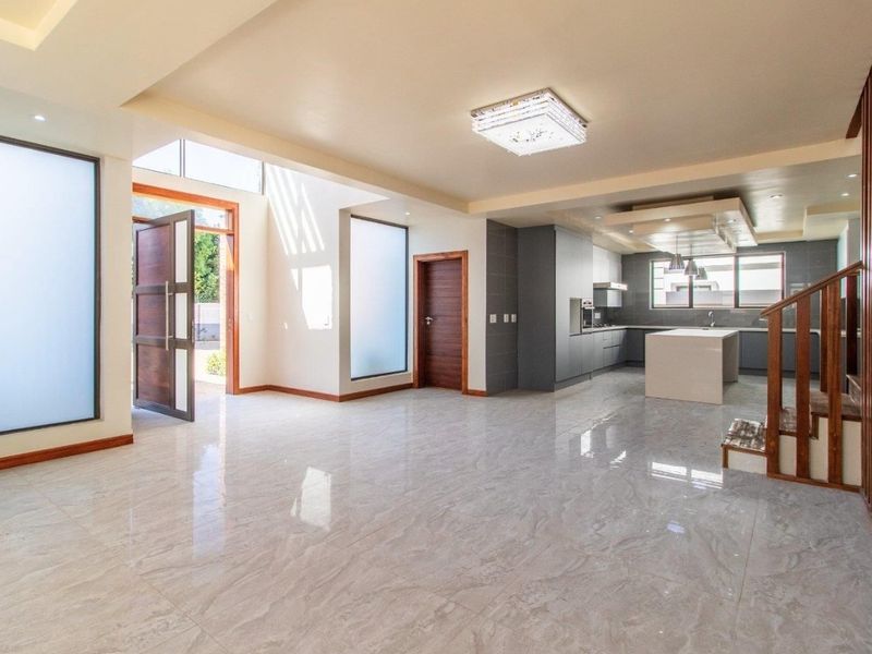 Spacious open-plan living area featuring polished porcelain tiles, a modern kitchen with a central island, and a wooden staircase leading to the upper level.