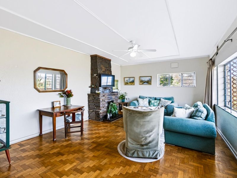 Spacious living room featuring a prominent stone fireplace, classic parquet flooring, and a ceiling fan, offering a warm and traditional atmosphere.
