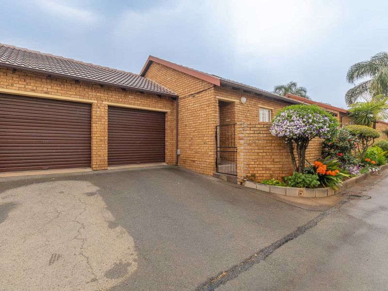 Front exterior view of a townhouse featuring a double garage, brick facade, and a paved driveway with an adjacent landscaped garden bed.