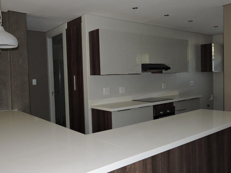 Modern kitchen featuring sleek cabinetry, stone countertops, integrated electric hob, oven, and a functional breakfast bar area.