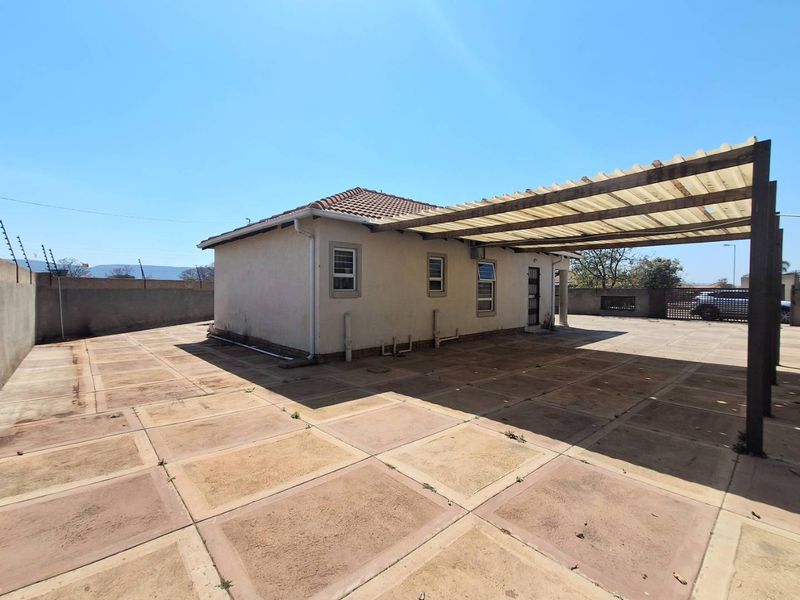 Rear exterior view of the property featuring a large paved courtyard, a covered pergola area, and secure perimeter walling with electric fencing.