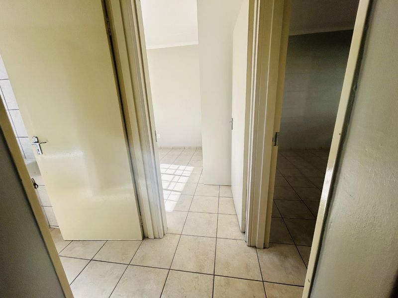 A view through a hallway connecting multiple empty rooms, featuring neutral tiled flooring and standard internal door frames.