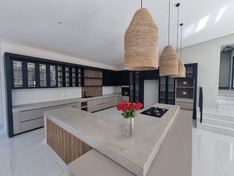 Modern kitchen featuring a large concrete island with a gas hob, sleek cabinetry, and stylish slatted wood accents, creating a sophisticated and functional culinary space.