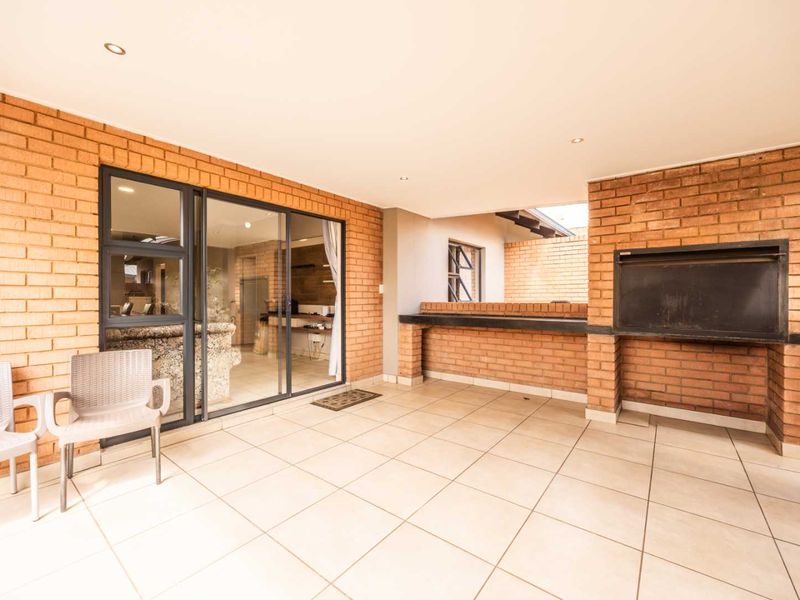 Covered patio featuring a built-in braai, tiled flooring, and sliding glass doors providing seamless access to the interior living space.