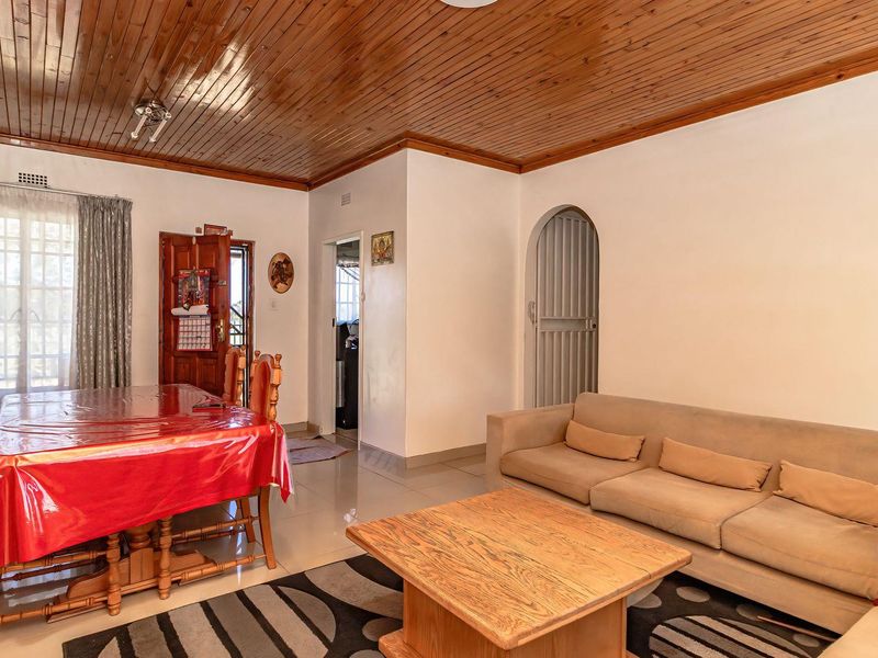 Open plan living and dining area featuring a timber tongue and groove ceiling, tiled flooring, and an arched doorway leading to other sections of the home.