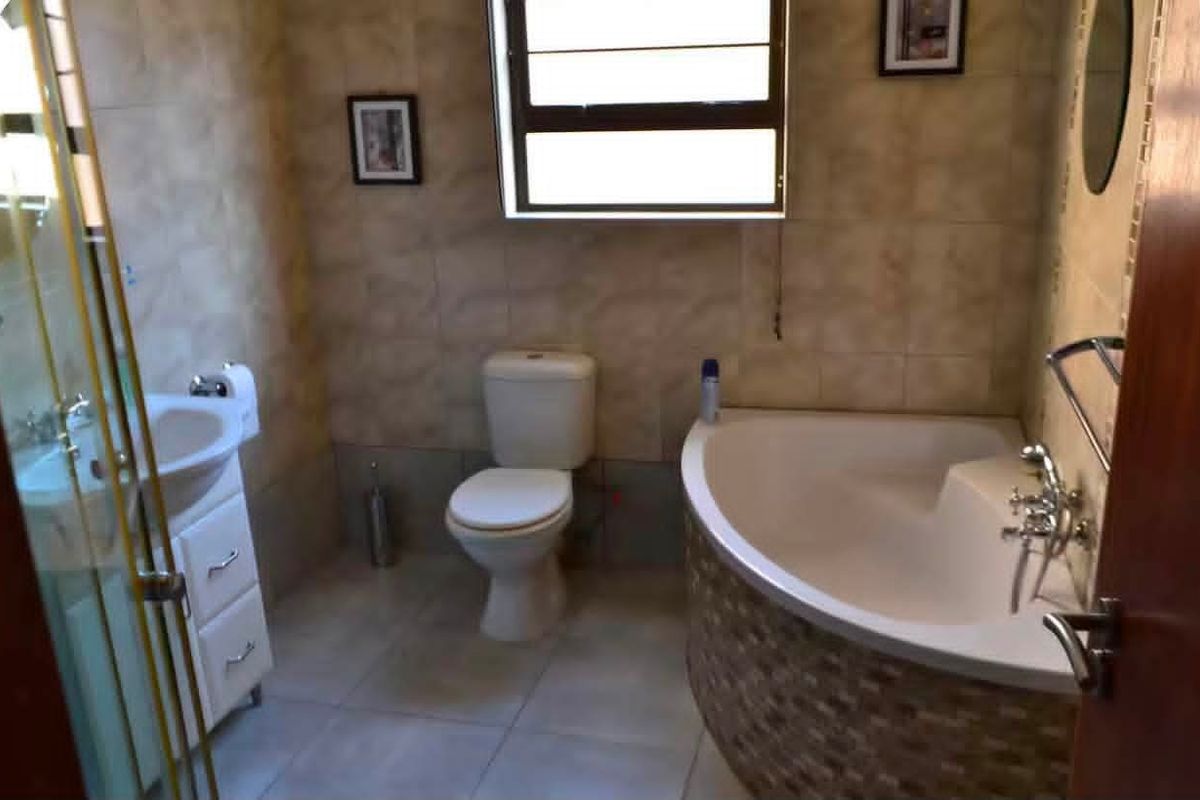 A functional bathroom featuring a corner bathtub, a vanity cabinet with integrated sink, a toilet, and a separate shower enclosure with tiled finishes.
