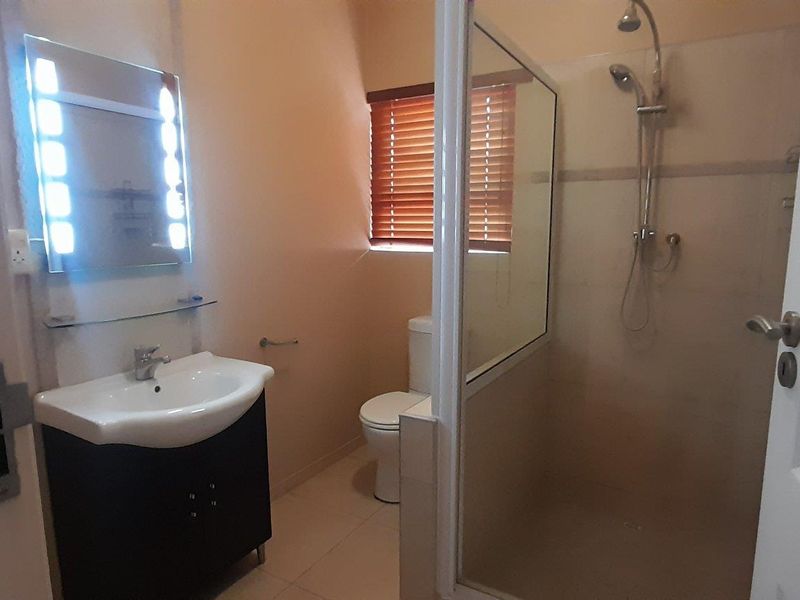 A clean, functional bathroom featuring a vanity with an illuminated mirror, a separate shower enclosure, and a toilet with privacy blinds.