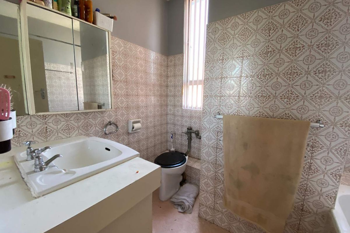 A dated bathroom featuring patterned wall tiles, a vanity with integrated basin, and a standard toilet, requiring modernization to improve its aesthetic appeal.