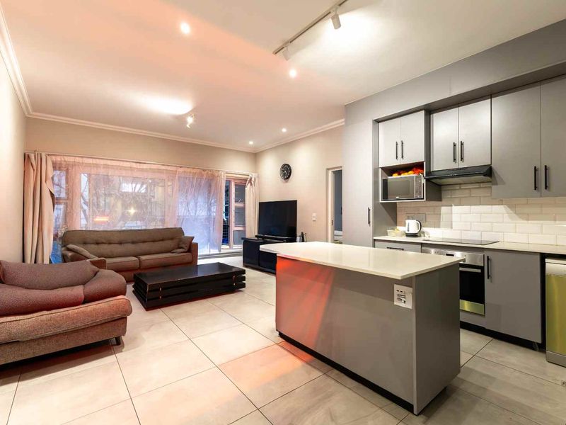 Open-plan living area featuring a modern kitchen with a central island, built-in appliances, subway tile backsplash, and neutral tiled flooring throughout.