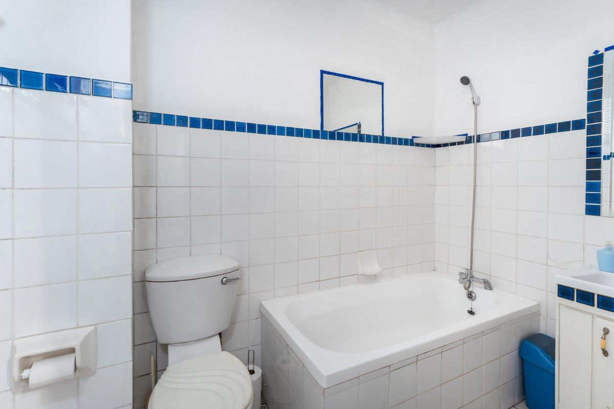 A functional bathroom featuring a bathtub with shower attachment, a toilet, and a vanity cabinet with tiled walls and blue accent detailing.