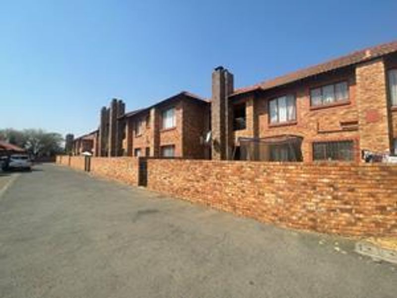 Exterior view of a face-brick cluster complex featuring tiled roofing, chimney stacks, and a perimeter boundary wall along the street.