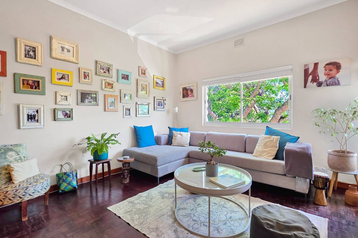 A bright and inviting living room featuring warm parquet flooring, a large sliding window, and classic cornice detailing.
