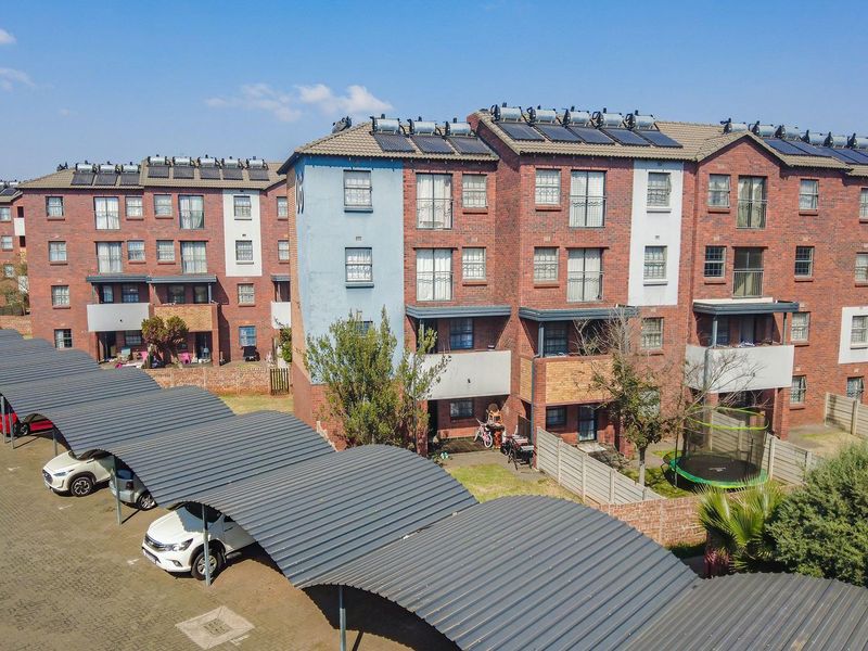 Aerial view of a multi-story apartment complex featuring brick facades, solar water heating systems, and covered parking bays.