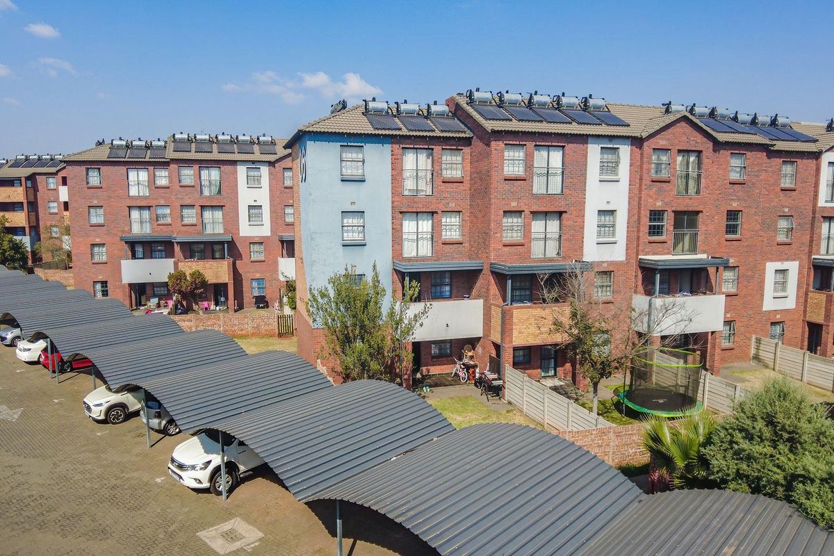Aerial view of a multi-story apartment complex featuring brick facades, solar water heating systems, and covered parking bays.
