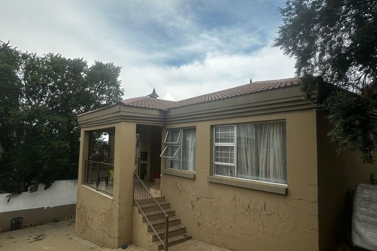 Exterior view of the house featuring a covered patio, concrete staircase, and tiled roof, showing signs of weathered plaster and paint.